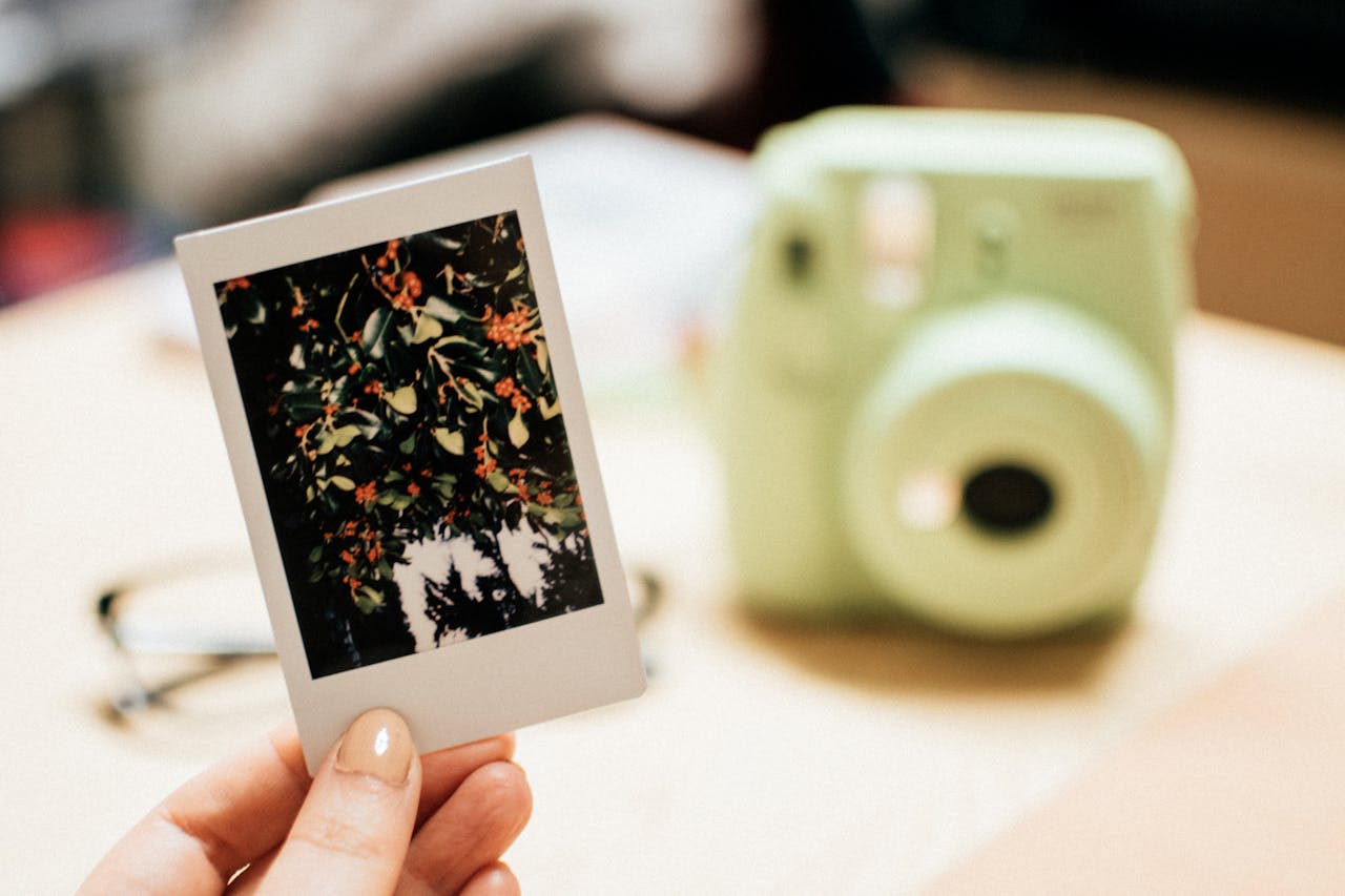 mobile-01 Hand holding an Instax photo of orange berries with blurred instant camera in the background.